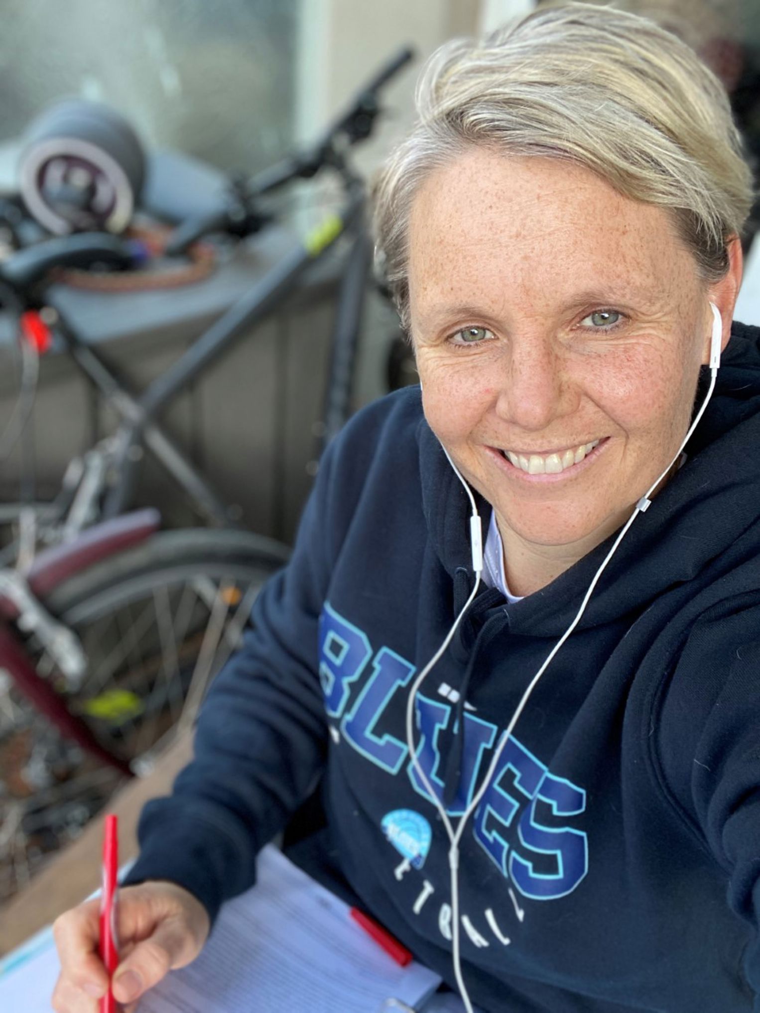 Selfie of Peta smiling while writing on her front porch in a hoodie with headphones in