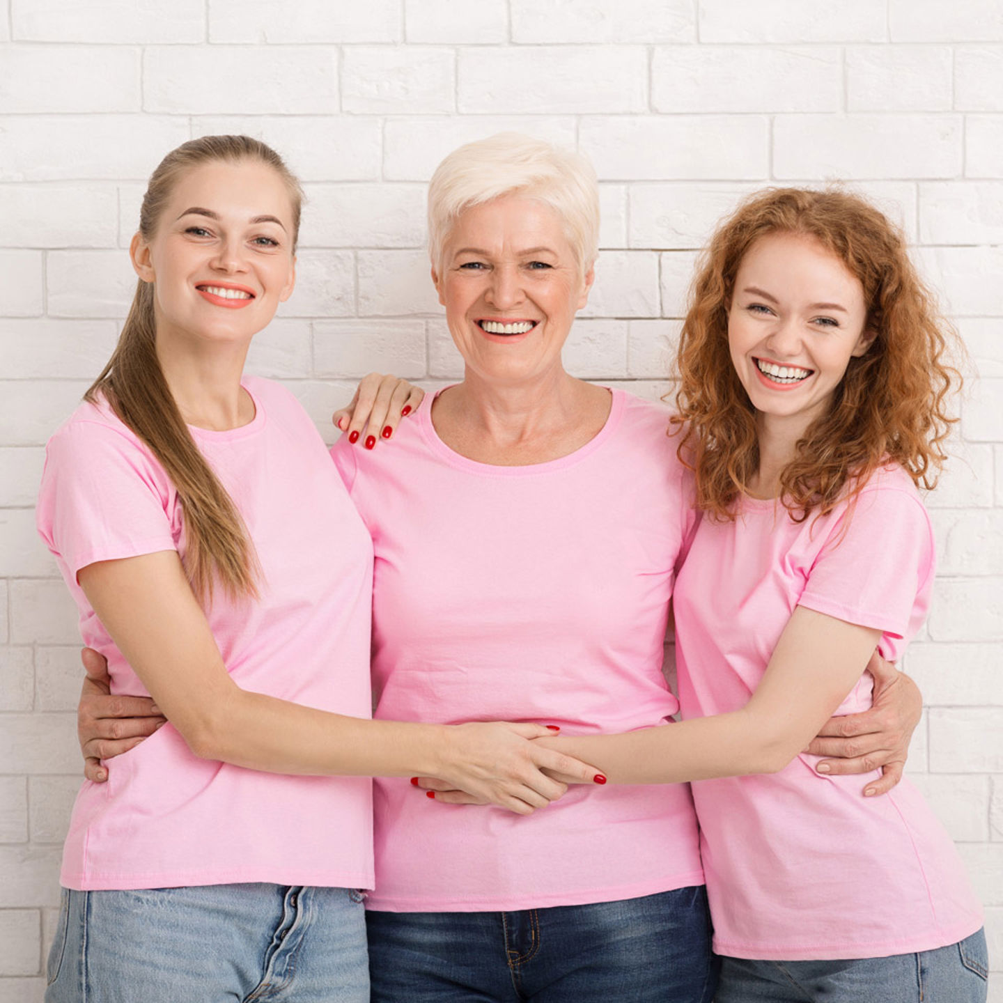Three women in pink shirts standing together with their arms around eachother