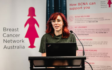 Dr Tonia Mezzini is giving a talk at a conference with the BCNA banner behind her