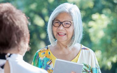 A woman with white hair and glasses is talking to someone while holding an iPad