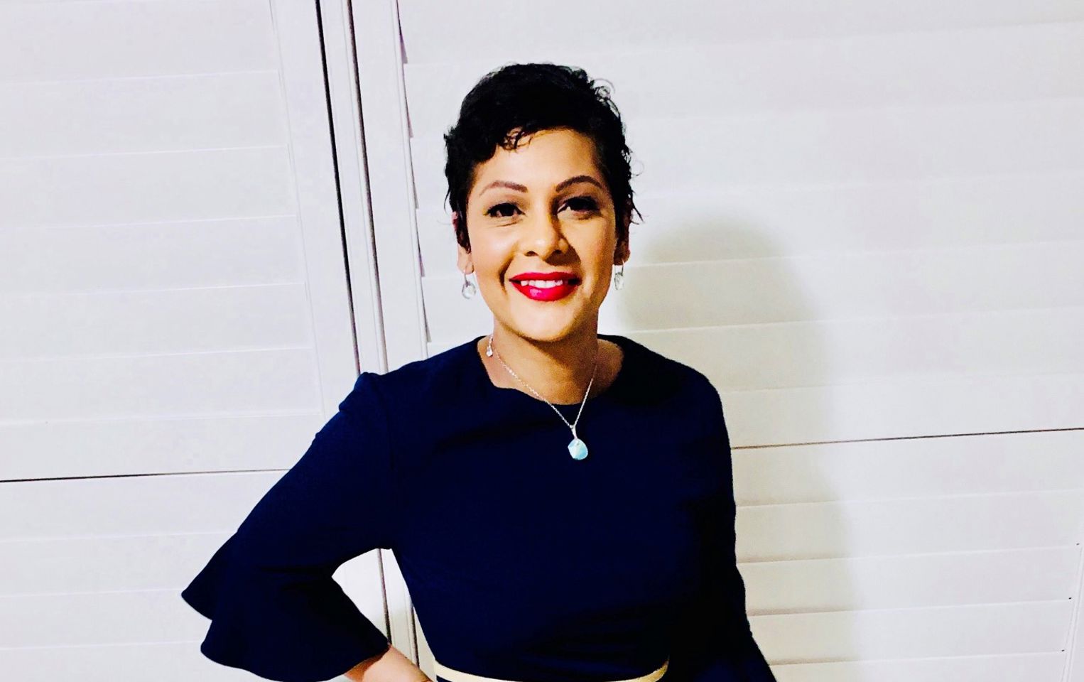 Nadine with her hand on hip, smiling at the camera with short hair