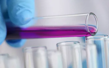 a closeup of someone wearing medical gloves, pouring liquid from one test tube into another