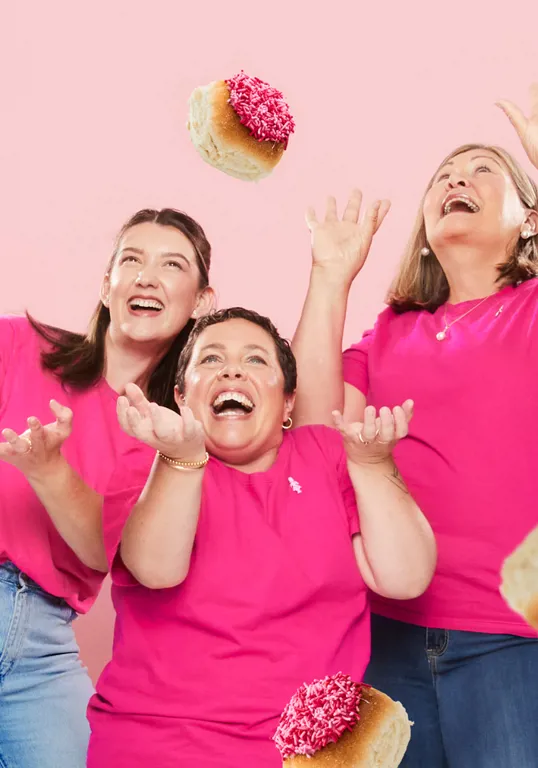 Three women in pink t-shirts laughing as pink buns rain down on them