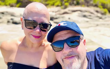 Jenny, who has breast cancer, wearing a strapless top and posing with her husband on a beach