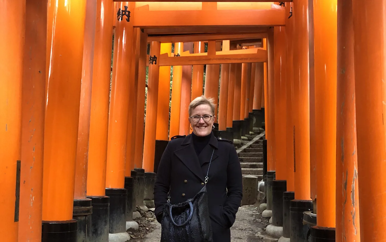 Alison standing under the orange arches in Japan in a black winter coat