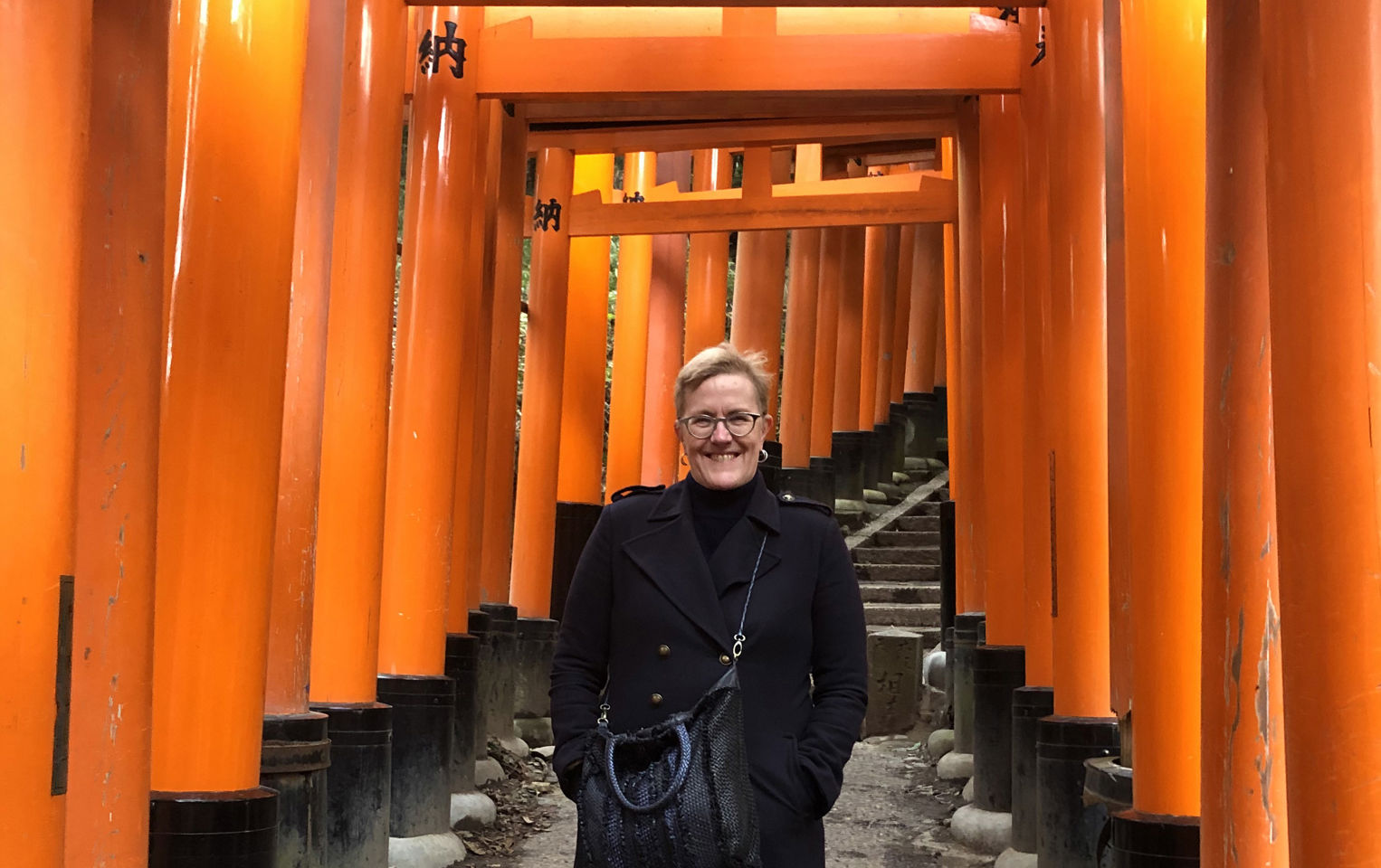 Alison standing under the orange arches in Japan in a black winter coat