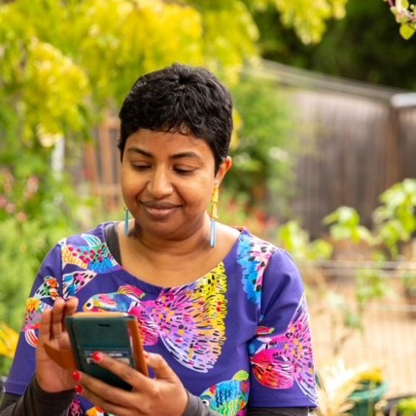 A woman is standing in a garden, looking at a mobile phone