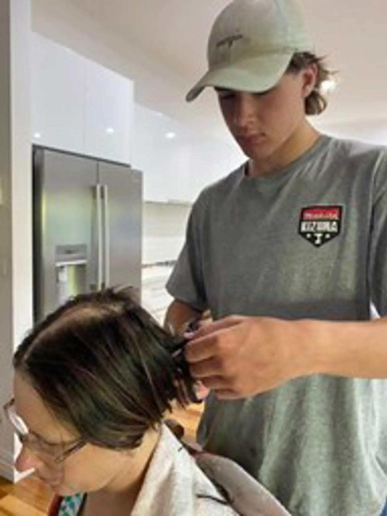 Tasha's teenage son, wearing a baseball cap, helps cut off his Mum's short, dark brown hair