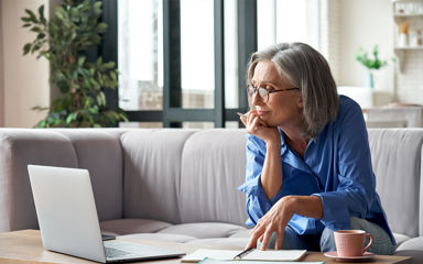 A mature older woman is sitting on the couch looking at a computer screen