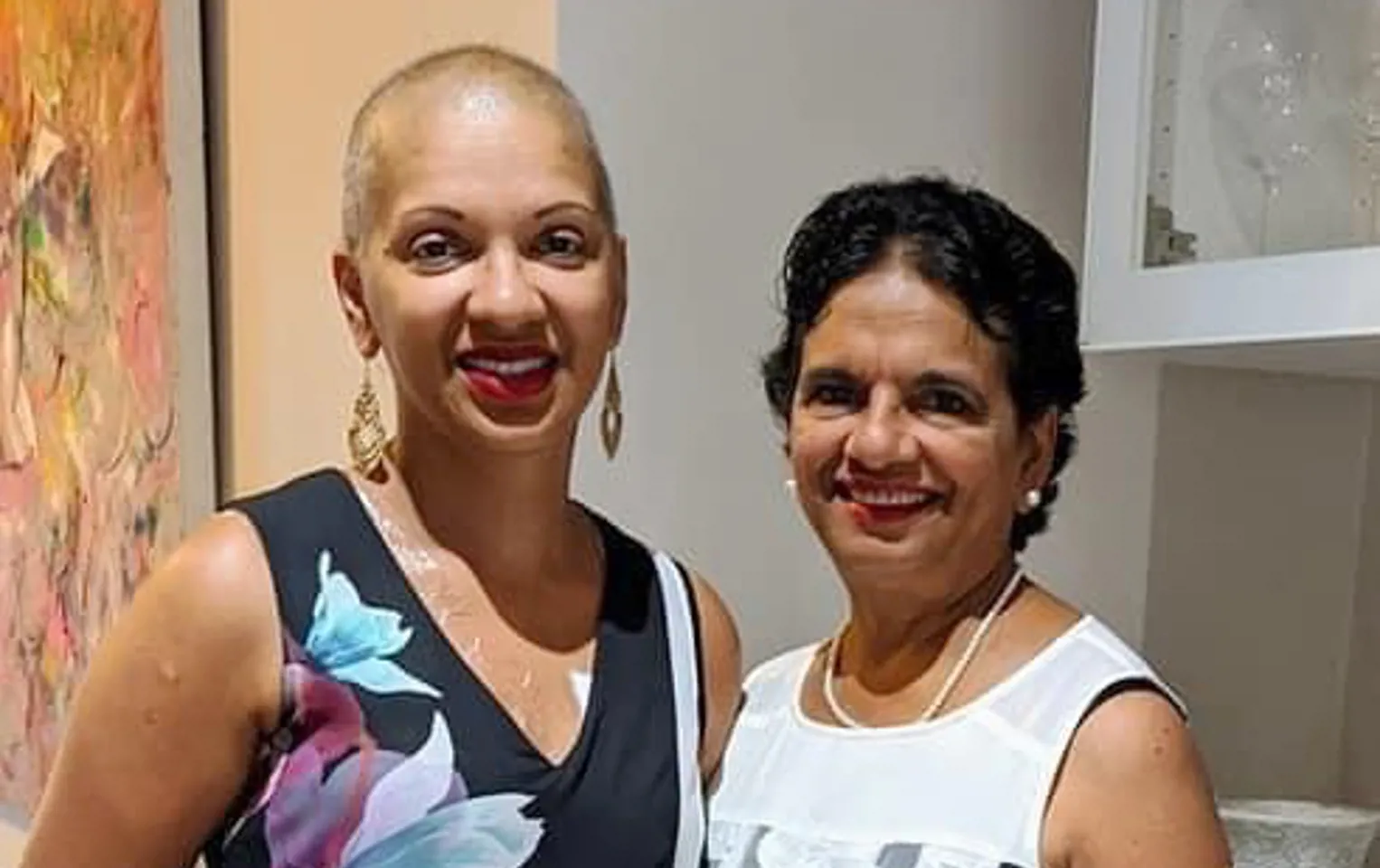 Dipthi with no hair in a floral dress standing next to her mother, they're both smiling at the camera