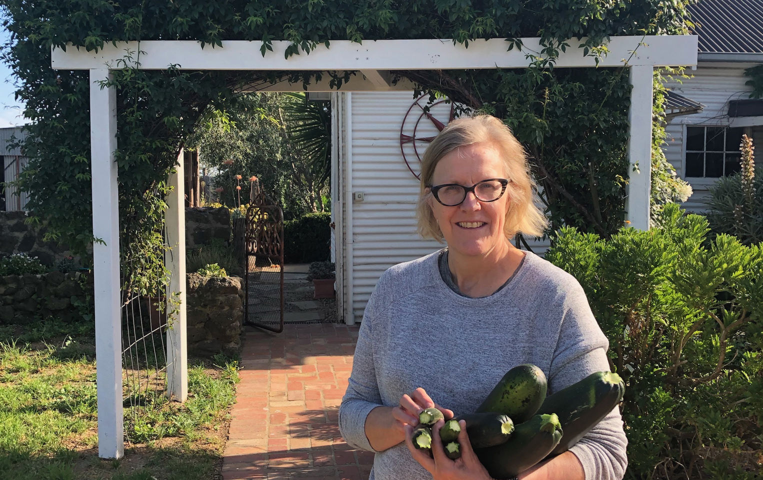 Alison in her garden holding a bunch of fresh picked zucchinis