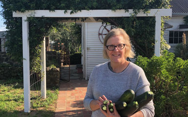 Alison standing her garden holding a bunch of freshly picked zucchini