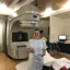 Megan stands beside hospital scanning machine. She is smiling and giving two thumbs up