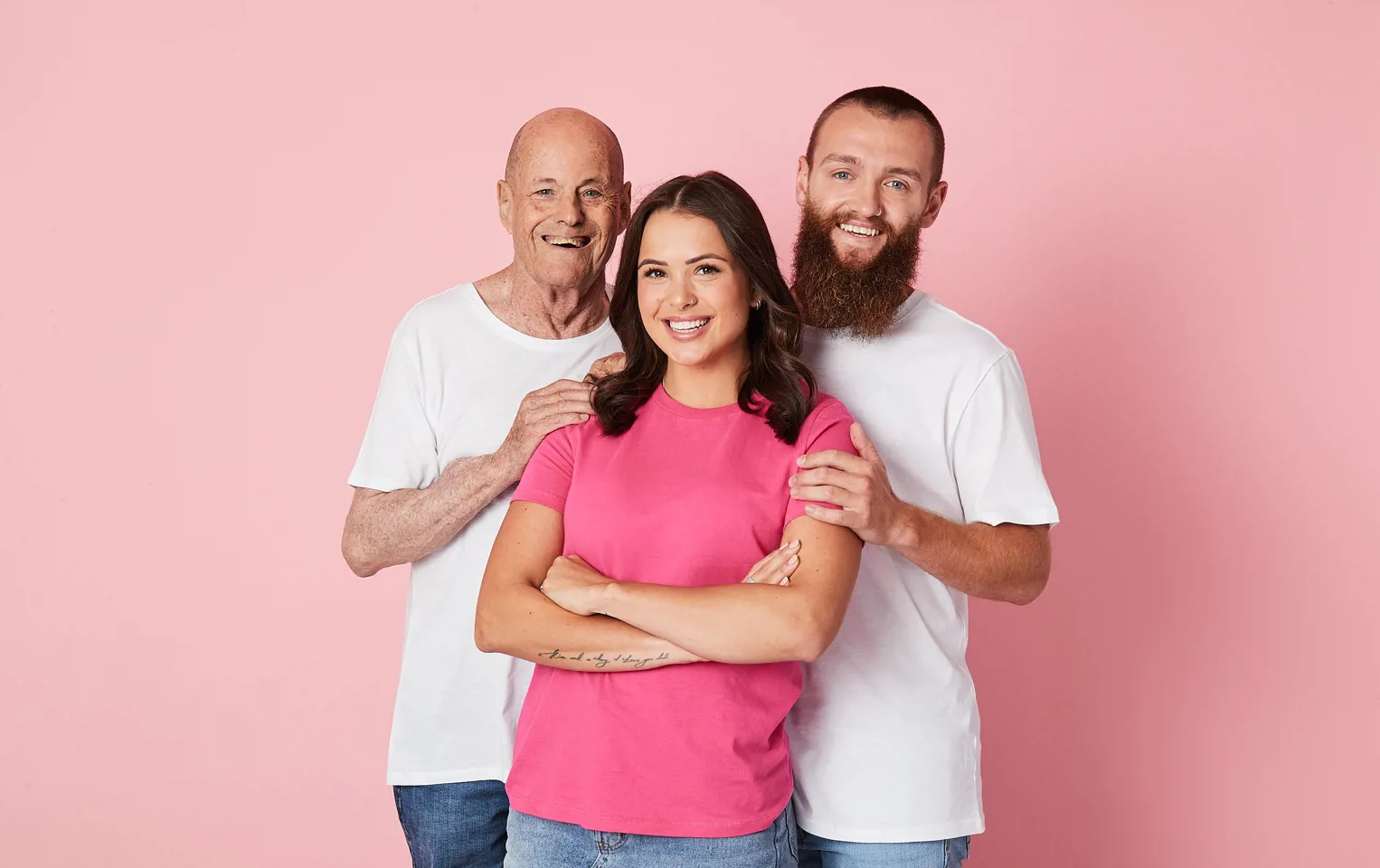 Stephanie wearing a pink top smiling at the camera with her father and partner standing behind her with their hands on her shoulder