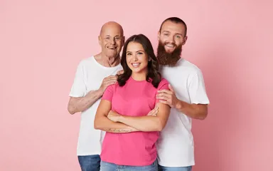 Stephanie wearing a pink top smiling with her father and partner behind her, their hands on her shoulder