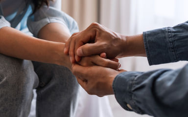 Close-up photo of two people holding hands in a caring manner