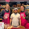 Jarrod & Thomas Berry standing with a Bakers Delight staff member in pink aprons