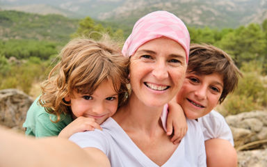 Woman in a headscarf taking a selfie of her and her two young sons in front of a beautiful green countryside vie