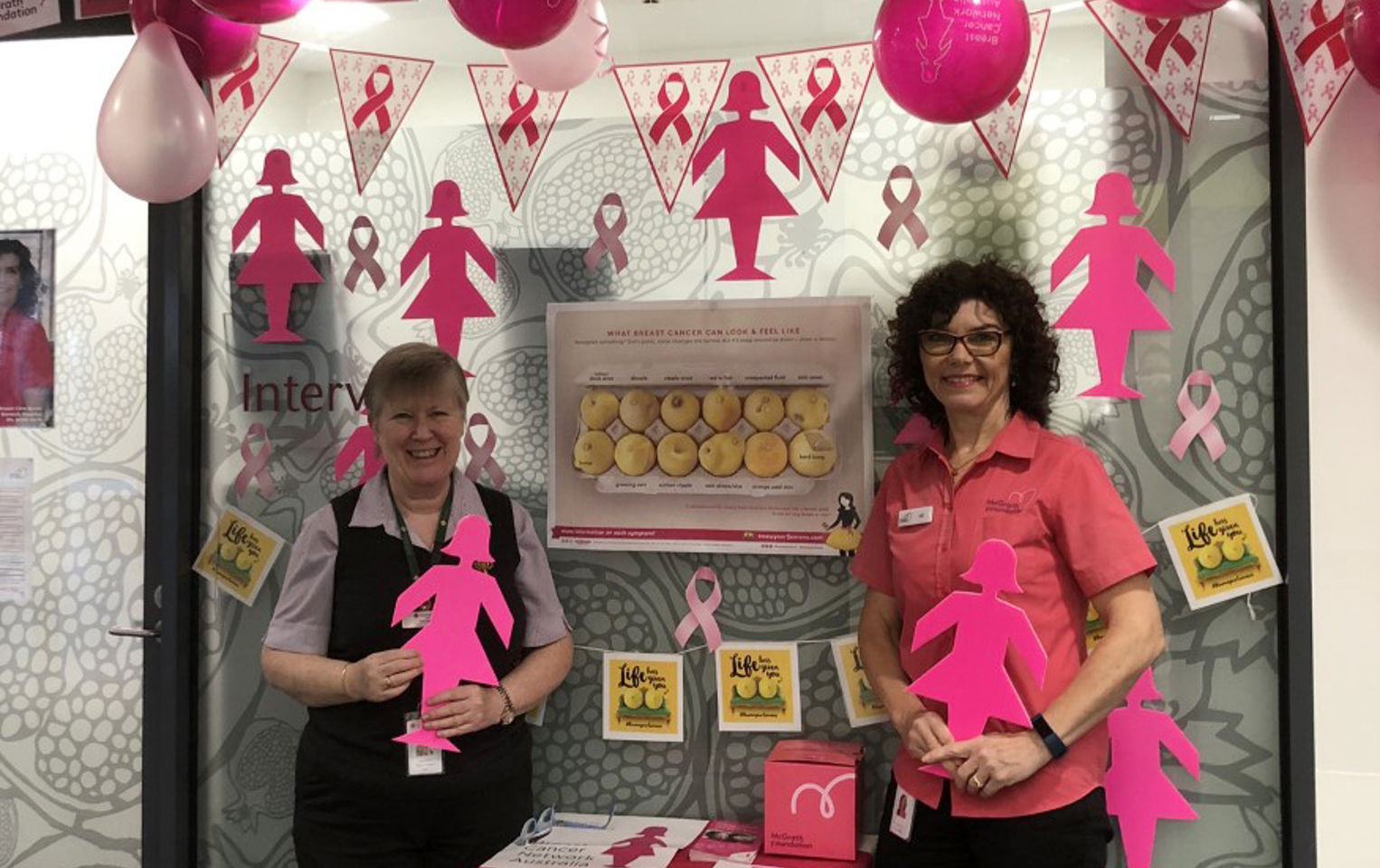 Maryanne and her colleague are standing amongst an array of pink lady silhouettes and pink ribbons for breast cancer awareness month, the day her life changed