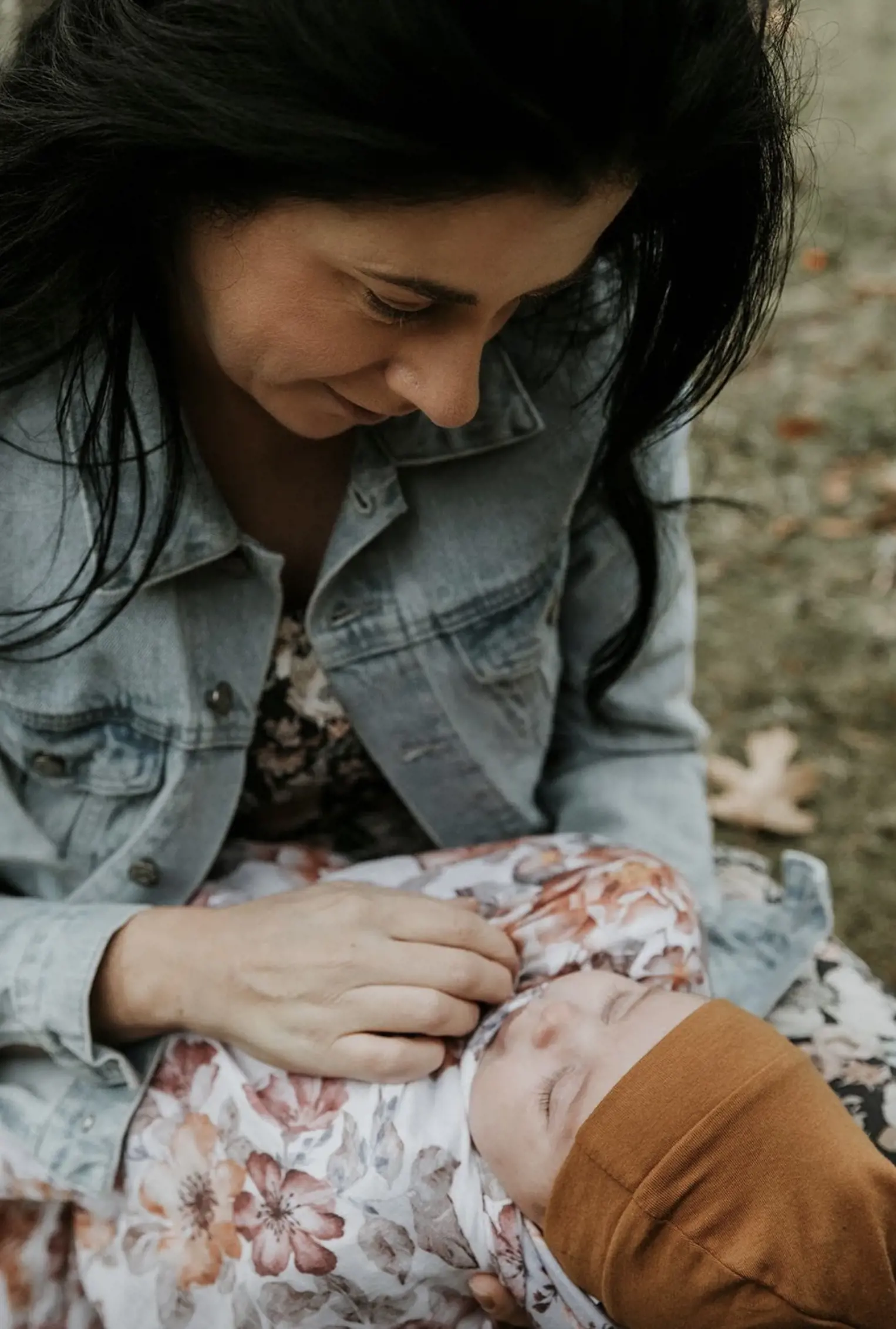 Shananne, with long dark hair and a denim jacket, is holding her baby
