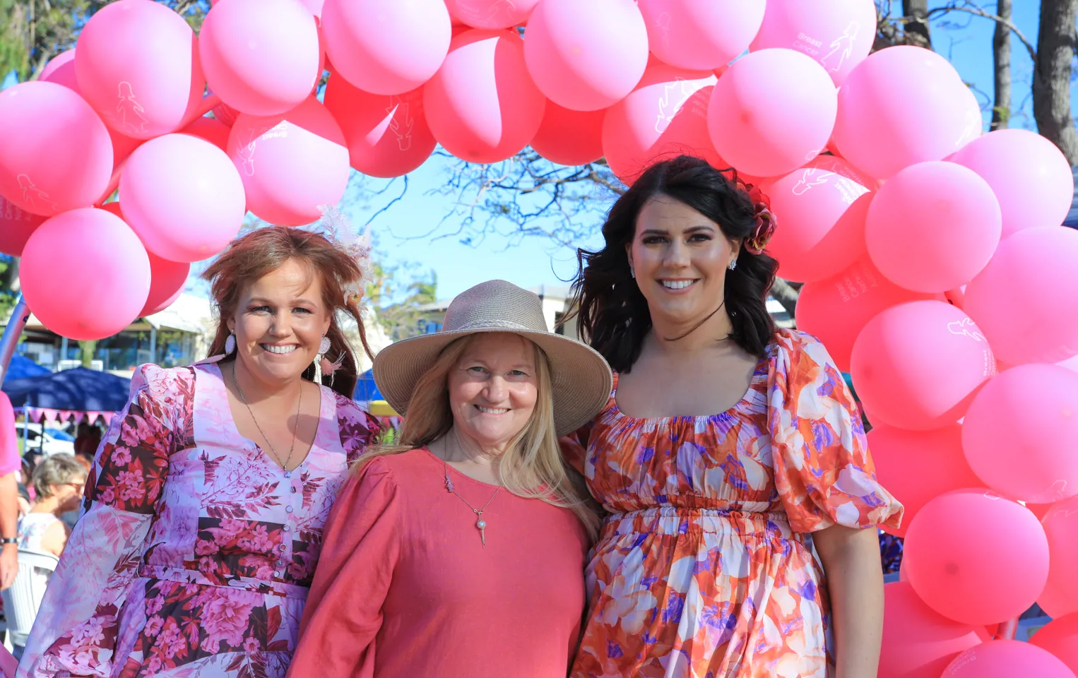 Three ladies under pink balloon garland 