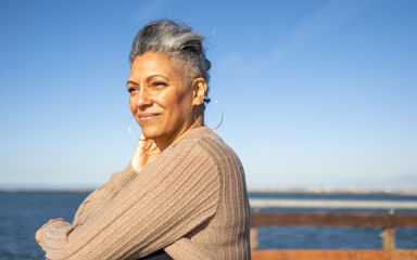 A mature woman is standing at the end of a pier, she appears deep in thought as she looks out over the water