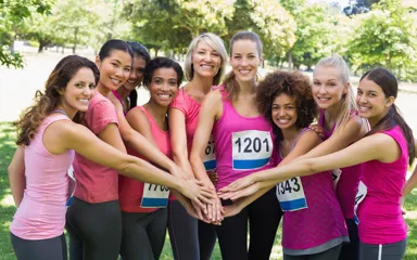 A group of people in activewear with race bibs, holding their hands in the middle of a semi-circle formation