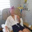 Lauren sitting in a hospital chair receiving treatment. She's wearing a pink and white headscarf and smiling with her thumbs up