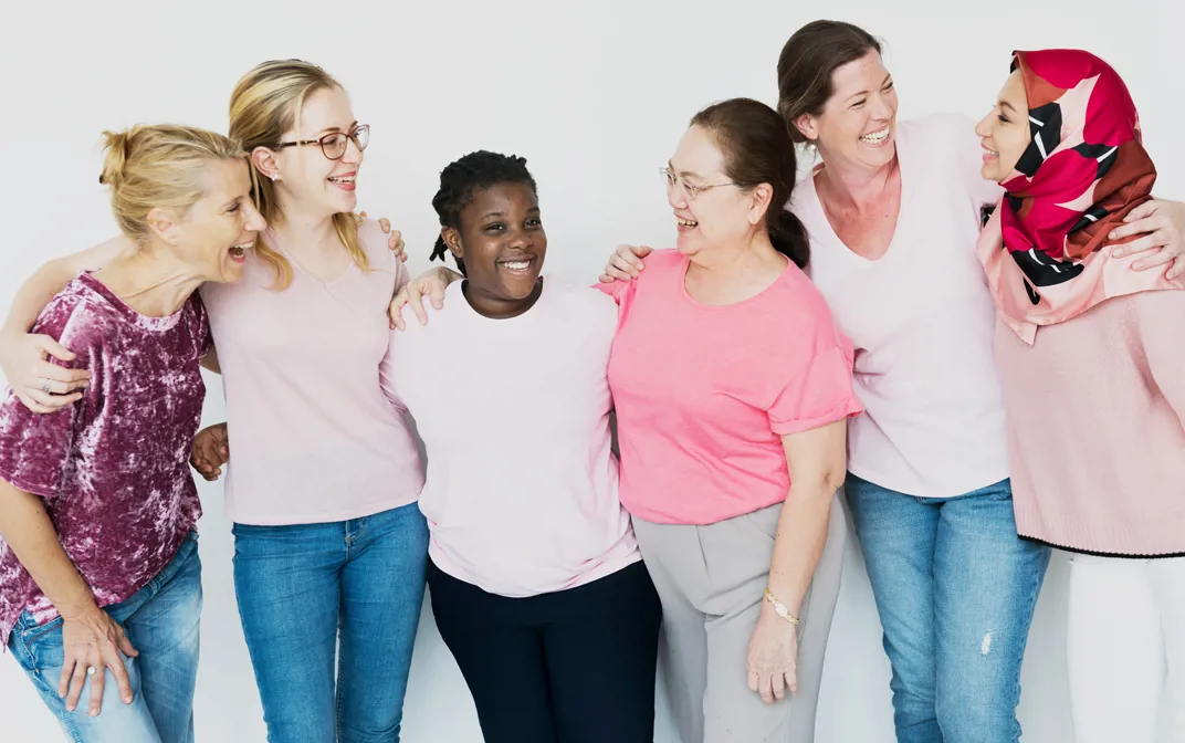 A group of multiethnic women wearing pink shirts, standing together with their arms around each other