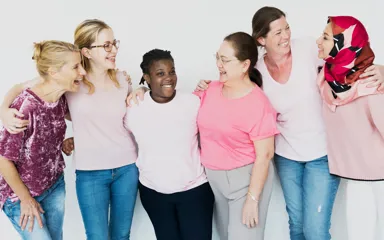 A group of multiethnic women wearing pink shirts, all standing together with their arms around each other