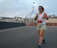 Sarah is running next to the Parliament of Australia. She is smiling.