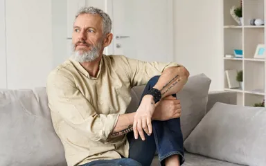 A man is sitting on the couch looking away from the camera in thought