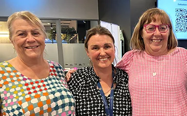 Image of three health professionals standing close together and smiling at the camera