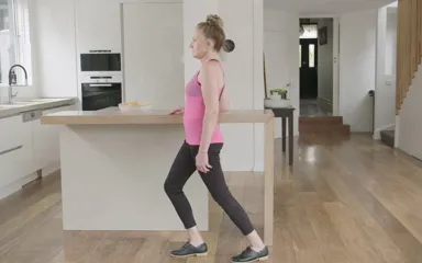 A woman is exercising in her kitchen, standing against her kitchen bench